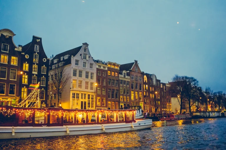 Boat on a canal beside lit houses in the evening