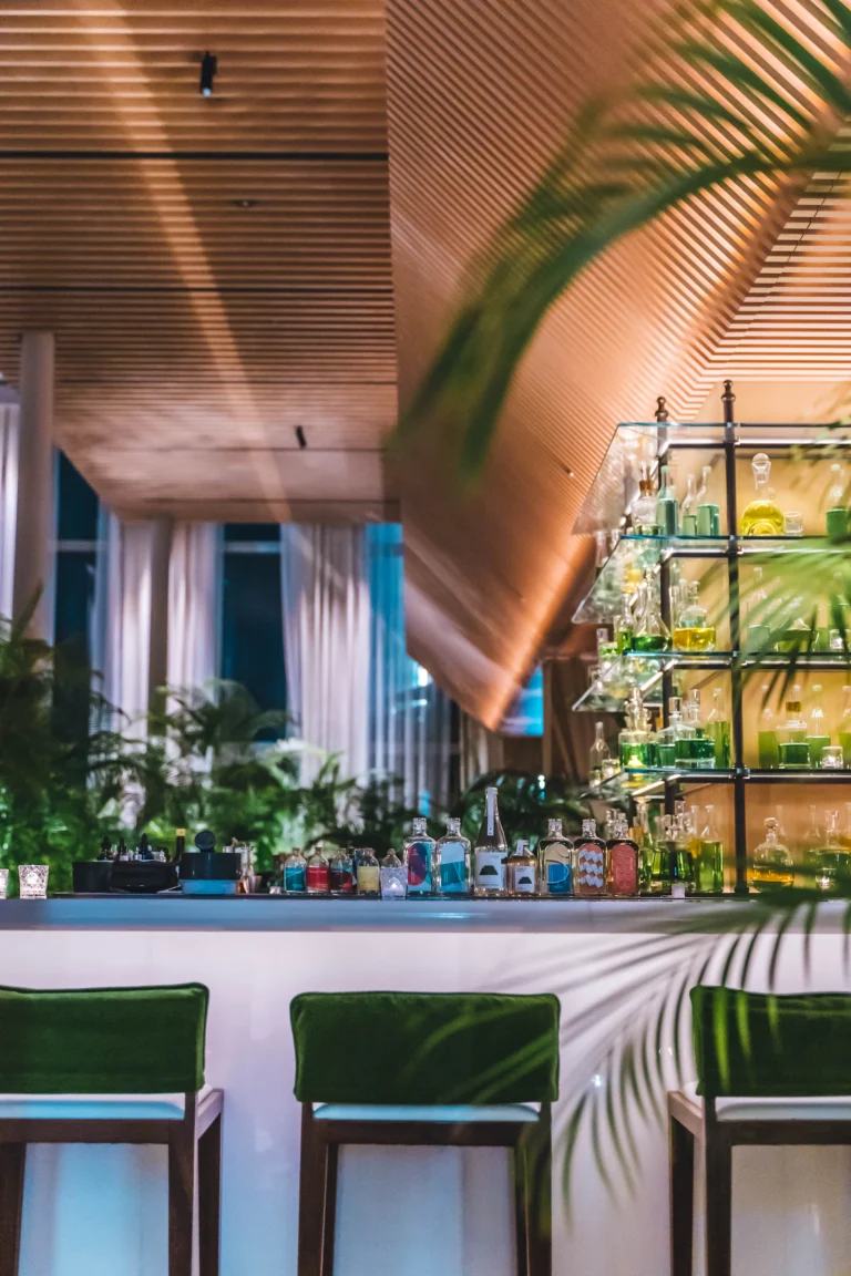 Hotel bar with warm lighting, plants and a shelf of bottles